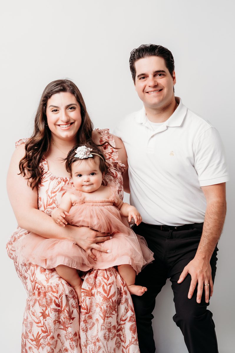 Parents holding their one-year-old daughter in a pink tulle dress during a first birthday portrait session at Kelli Dease Photography in Farmington, CT