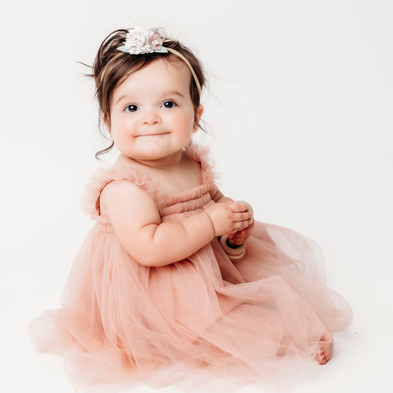 Baby girl in a pink tulle birthday dress smiling at the camera during her first birthday milestone session at Kelli Dease Photography
