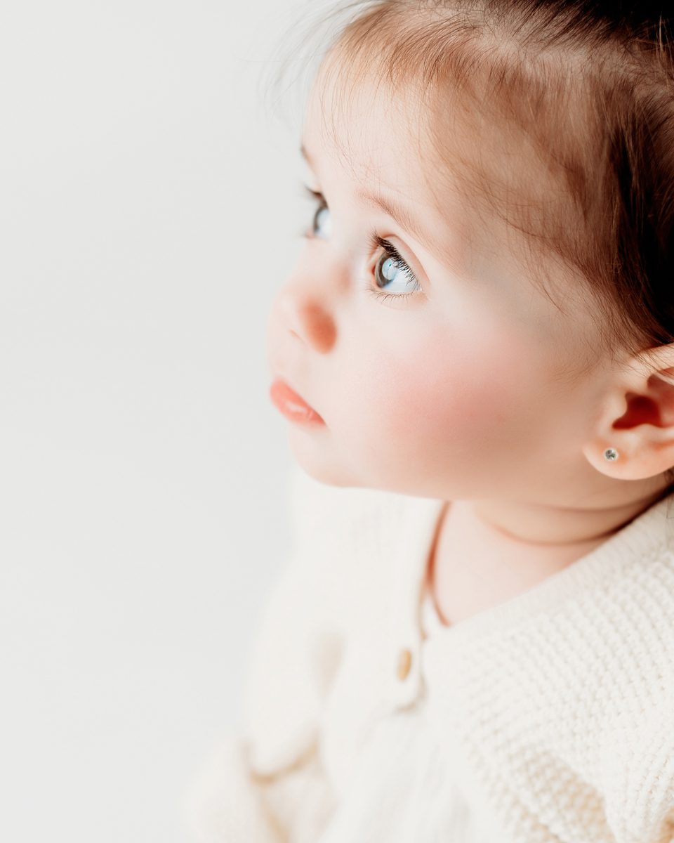 Close-up profile of a baby in a cream knit outfit during a studio milestone session at Kelli Dease Photography in Farmington, CT.