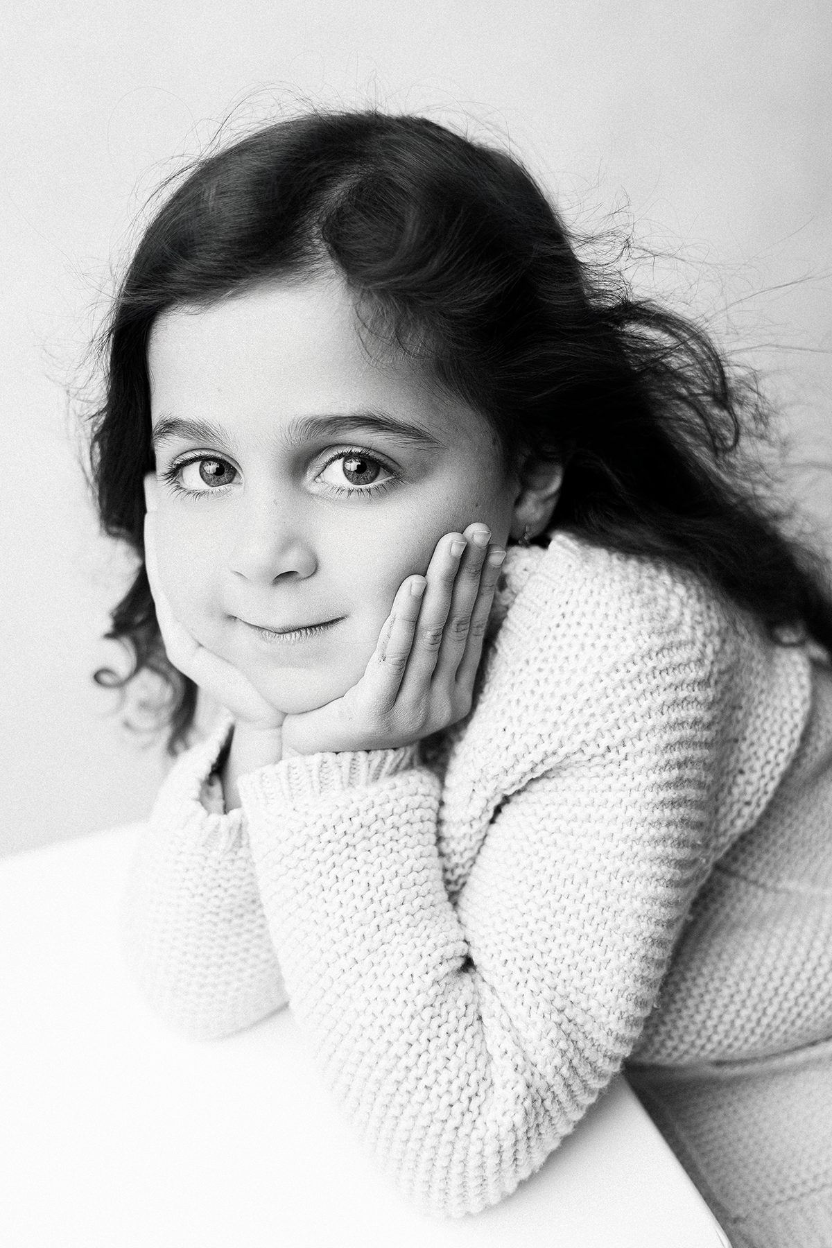 Young girl resting chin on hands in cozy sweater, black and white studio portrait, Kelli Dease Photography