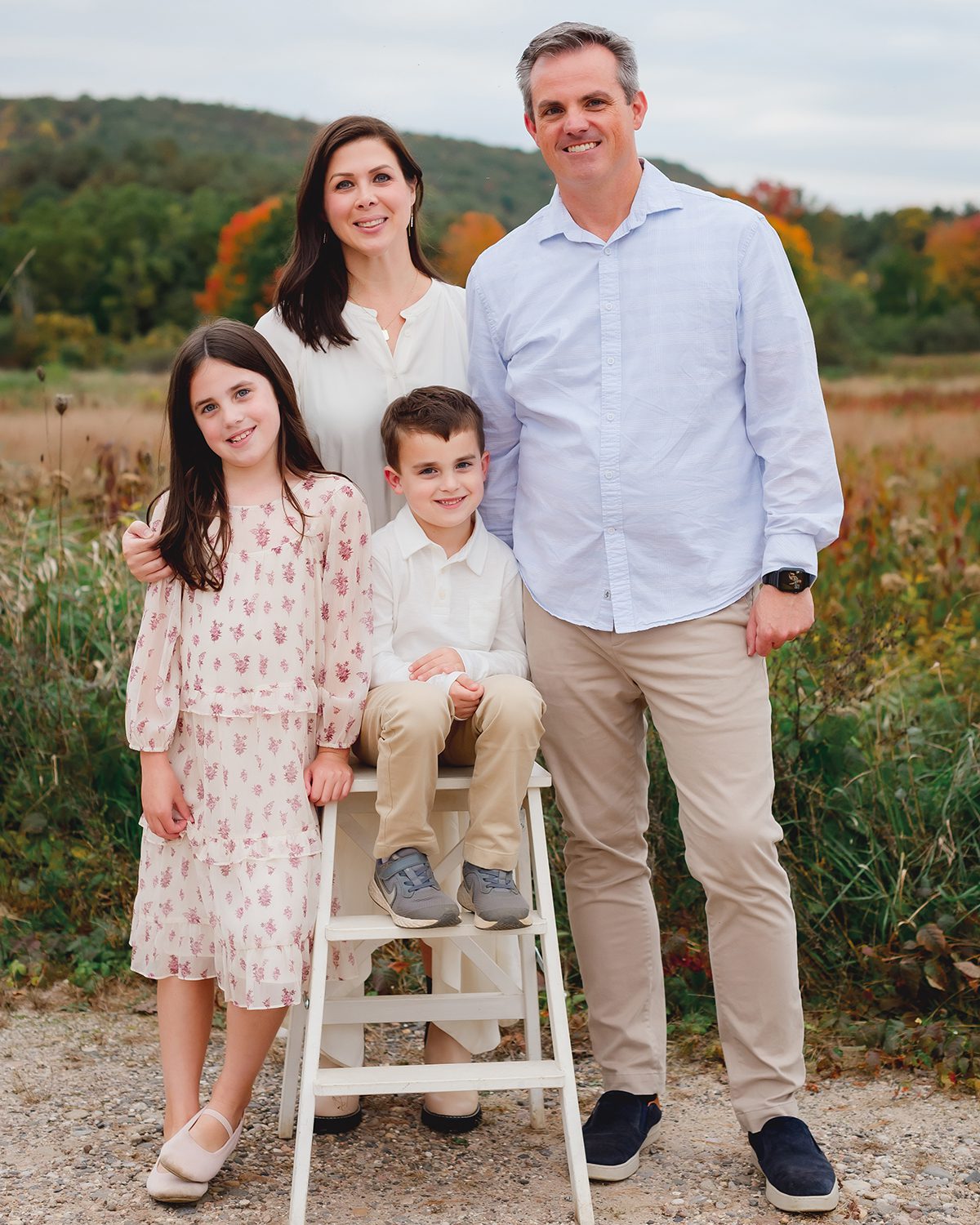 Family of four in cream and pale blue standing together in a Connecticut field during a fall family session with Kelli Dease Photography