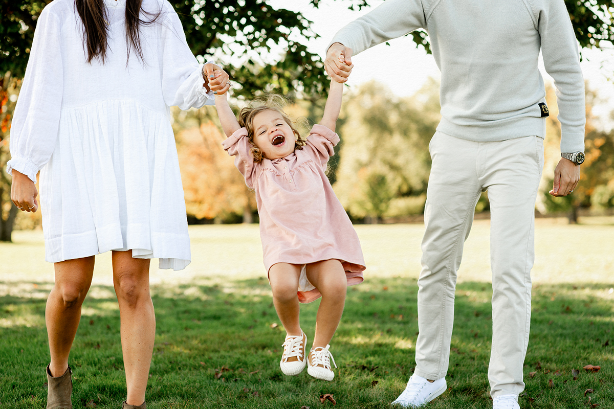 Parents playing with a toddler girl dressed in a pink dress during an outdoor family photo session in Connecticut